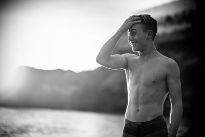 Shirtless smiling teenage boy looking away while standing at beach