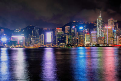 Illuminated city by sea against sky at night