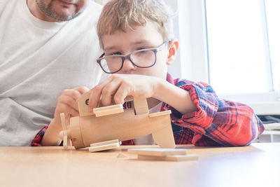 Cute boy building model airplane at home