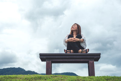 Low angle view of woman sitting on seat against cloudy sky