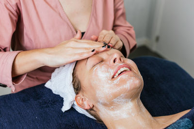Crop unrecognizable cosmetician applying facial cleanser on face of female client during skin care treatment in beauty salon