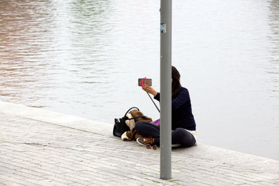 Full length of woman taking selfie while sitting against river