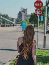 Rear view of woman with long blond hair walking on sidewalk