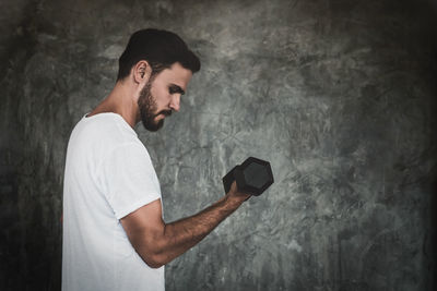 Side view of young man standing against wall