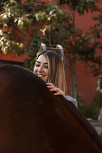 Young blonde woman with her brown horse enjoys a day on the farm.