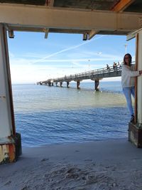 Woman standing on bridge over sea against sky