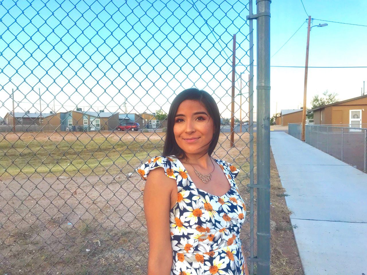 smiling, looking at camera, portrait, one person, front view, real people, leisure activity, standing, fence, happiness, young adult, lifestyles, casual clothing, emotion, young women, barrier, chainlink fence, architecture, sky, hair, outdoors, beautiful woman, hairstyle