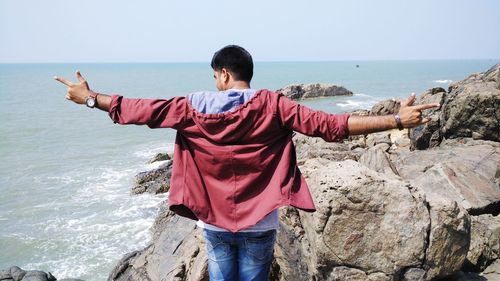 Rear view of man standing at beach against sky