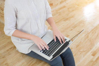 Midsection of woman using laptop on hardwood floor