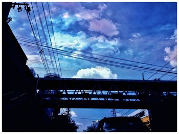 Low angle view of electricity pylon against cloudy sky