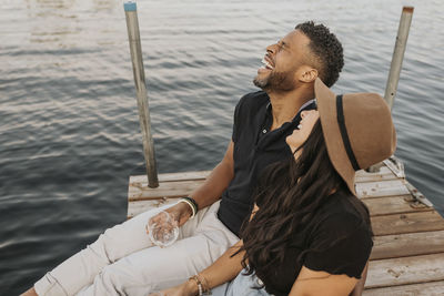 Happy couple drinking wine while sitting on pier