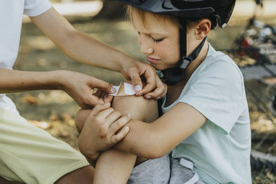 Boy putting bandage on younger brother knee sitting in public park