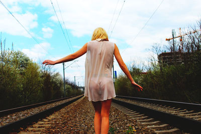 Rear view of woman standing by railroad tracks against sky