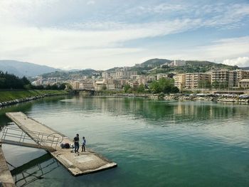 People walking by river against built structures