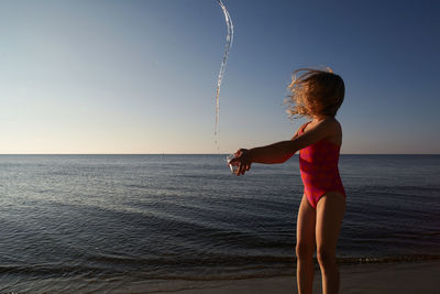 Cute girl throwing water at beach against sky