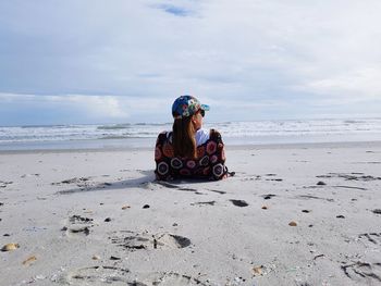 Rear view of woman lying on sand at beach against sky