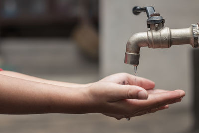 Close-up of hand collecting water falling from faucet