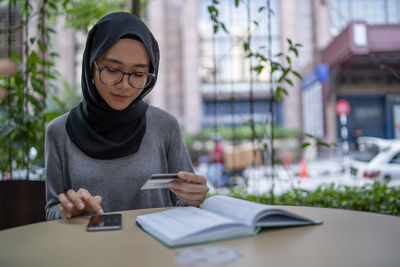 Young woman making mobile payment while sitting at sidewalk cafe in city