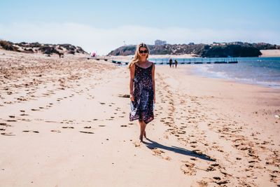 Portrait of young woman standing on beach against sky