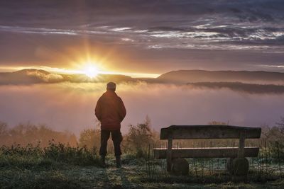 Rear view of man walking on field against sky during sunset