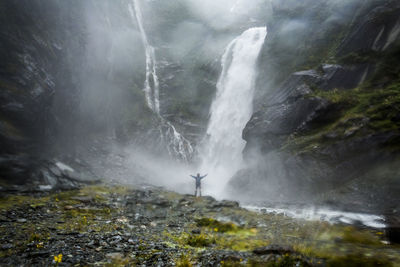 Figure standing in front of a raging waterfall in zealand