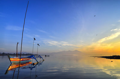 Sailboats moored in sea against sky during sunset