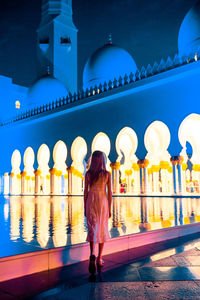 Rear view of woman walking by illuminated building at night