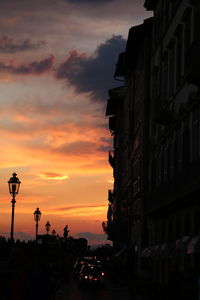 Silhouette city street against sky during sunset