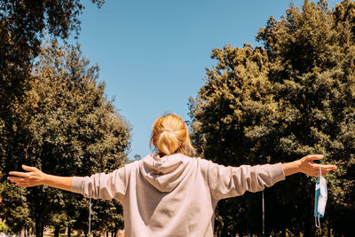 Rear view of woman with arms raised against trees