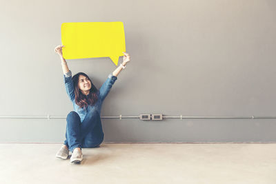 Portrait of woman with arms raised against wall