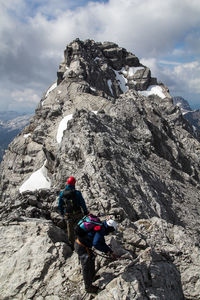 Rear view of man climbing on rocky mountain against sky