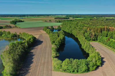 Aerial view of a small dark blue pond with high trees on the bank between fields