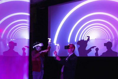 Colleagues with virtual reality glasses gesturing by projection screen at exhibition center