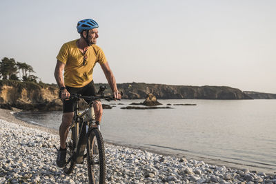 Smiling mature man riding bicycle at beach