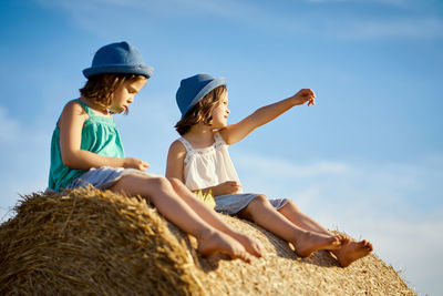 Low angle view of friends wearing hats sitting on hay bale against sky