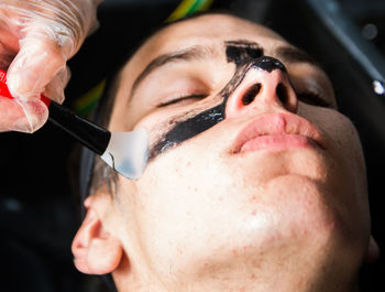 Cropped hand of beautician applying facial mask on teenage boy 