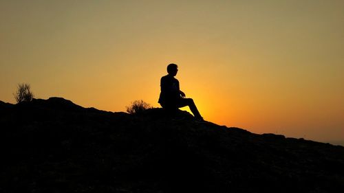 Silhouette man standing on rock against sky during sunset