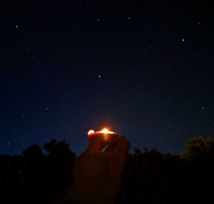 Person holding illuminated lighting against sky at night