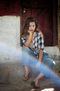 Portrait of a young woman sitting against brick wall