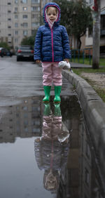 Little girl in warm clothes stands in the puddle