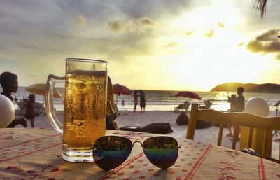 People on table at beach against sky during sunset