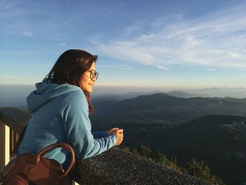 Side view of woman looking at landscape on mountain against sky during sunset