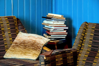 Two  armchairs stand in the corner of a blue-panelled room, a stack of books lies on a corner table.