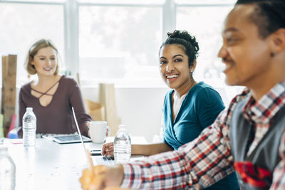 Happy businesswoman looking away while sitting by colleagues