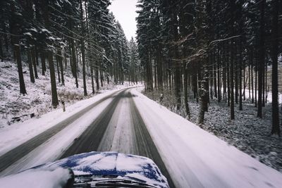 Road amidst trees on field seen through car windshield during winter