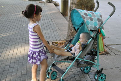 Sister holding feet of brother while standing on footpath