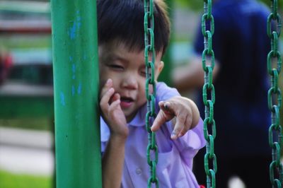 Cute boy winking while gesturing amidst outdoor play equipment at playground