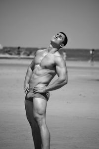 Shirtless muscular man standing at beach against clear sky