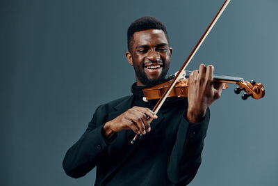 Portrait of young man playing violin against black background