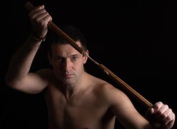 Portrait of shirtless man with knife against black background